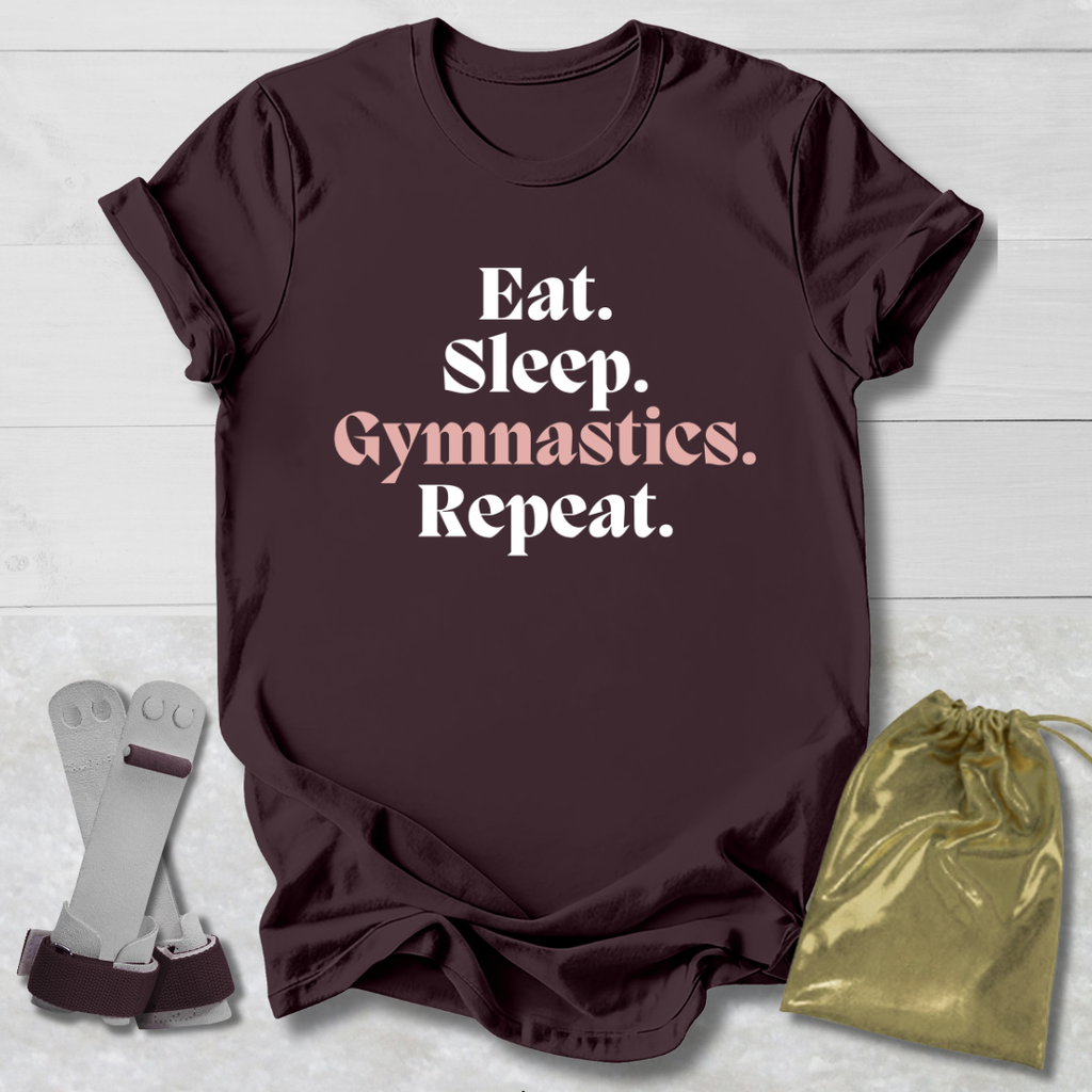 Brown t-shirt with 'Eat. Sleep. Gymnastics. Repeat.' text, socks, and drawstring bag on a light wooden surface.