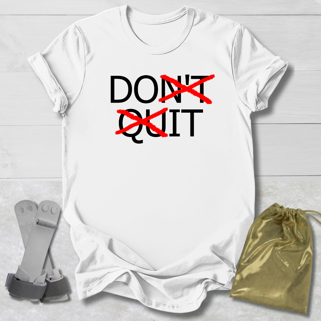 White t-shirt with 'DON'T QUIT' text on a light wooden surface with socks and a drawstring bag.