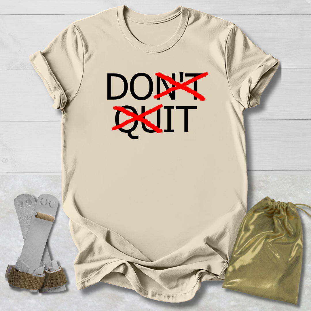 Beige t-shirt with 'DON'T QUIT' text, socks, and drawstring bag on a light wooden surface