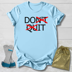 Light blue t-shirt with 'DON'T QUIT' text, socks, and drawstring bag on a wooden surface