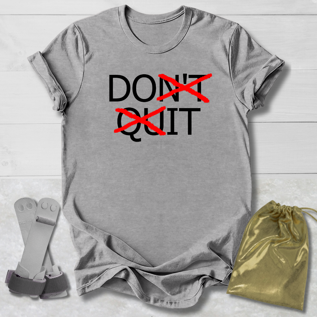Gray t-shirt with 'Don't Quit' text on a light wooden surface with socks and a drawstring bag.