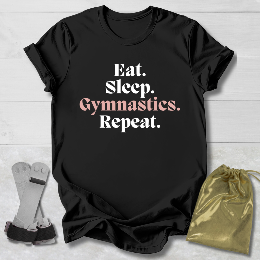 Black t-shirt with 'Eat. Sleep. Gymnastics. Repeat.' text on a light wooden surface with socks and a drawstring bag.
