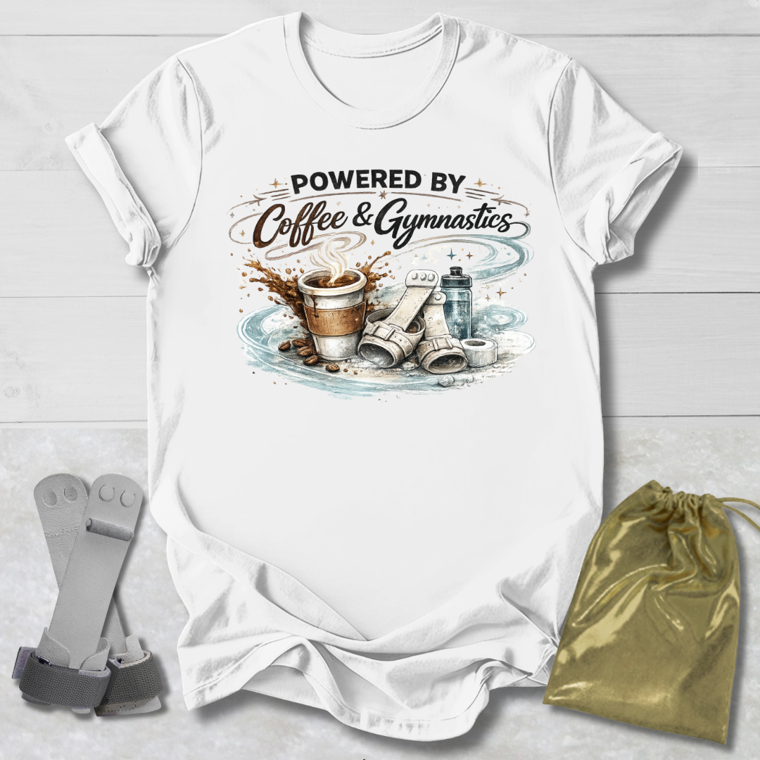 White t-shirt with 'Powered by Coffee & Gymnastics' design on a wooden surface with socks and a drawstring bag.