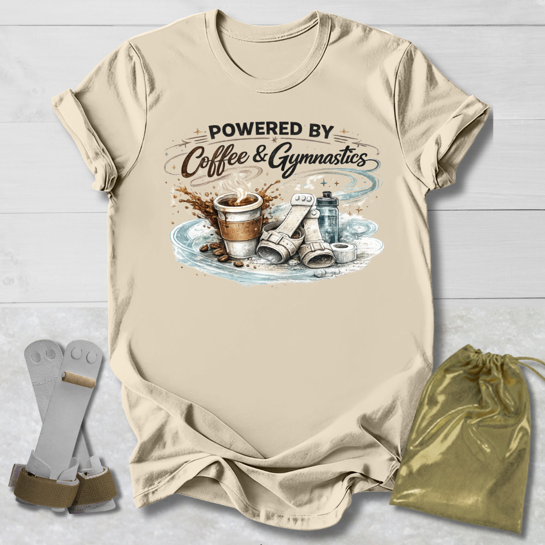 Beige t-shirt with 'Powered by Coffee & Gymnastics' graphic on a wooden surface with socks and a drawstring bag.