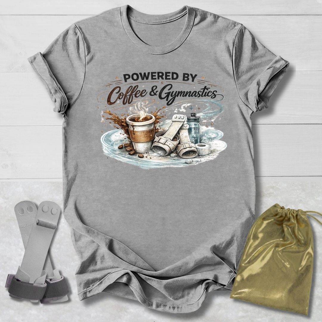 Gray t-shirt with 'Powered by Coffee & Gymnastics' graphic on a wooden surface with socks and a drawstring bag.