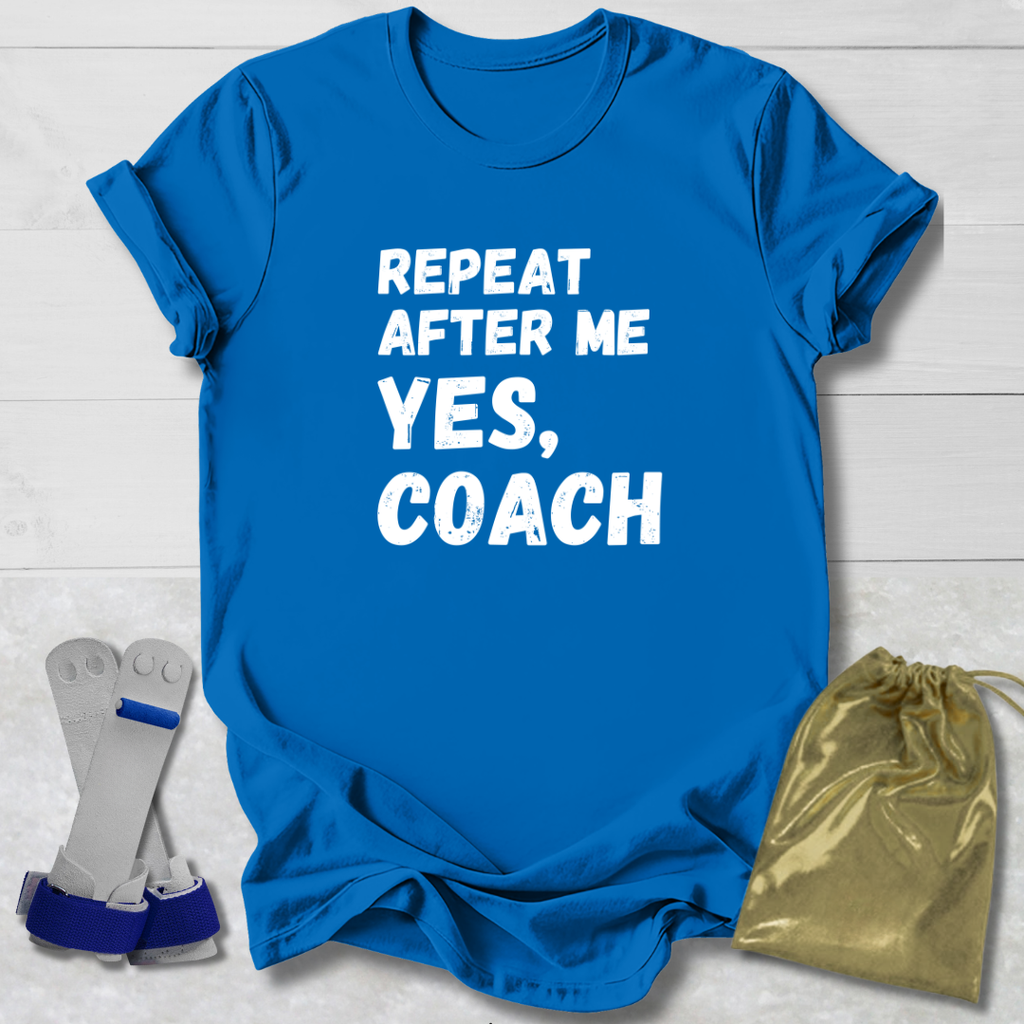 Blue t-shirt with 'Repeat after me yes, coach' text on a light wooden surface with socks and a drawstring bag.
