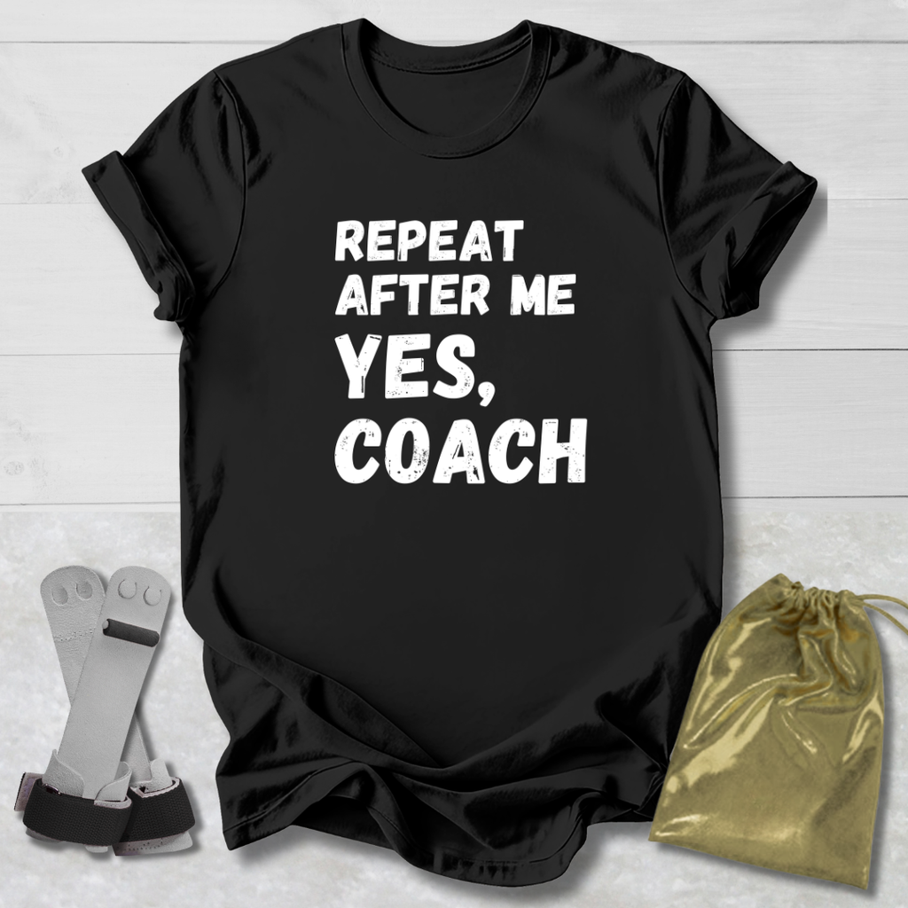 Black t-shirt with 'Repeat after me, yes, coach' text on a wooden surface with socks and a drawstring bag.