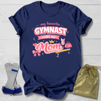 Navy blue t-shirt with pink gymnastics-themed design on a light wooden surface.