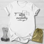 White t-shirt with gym-themed design and text, socks, and drawstring bag on a light wooden surface.