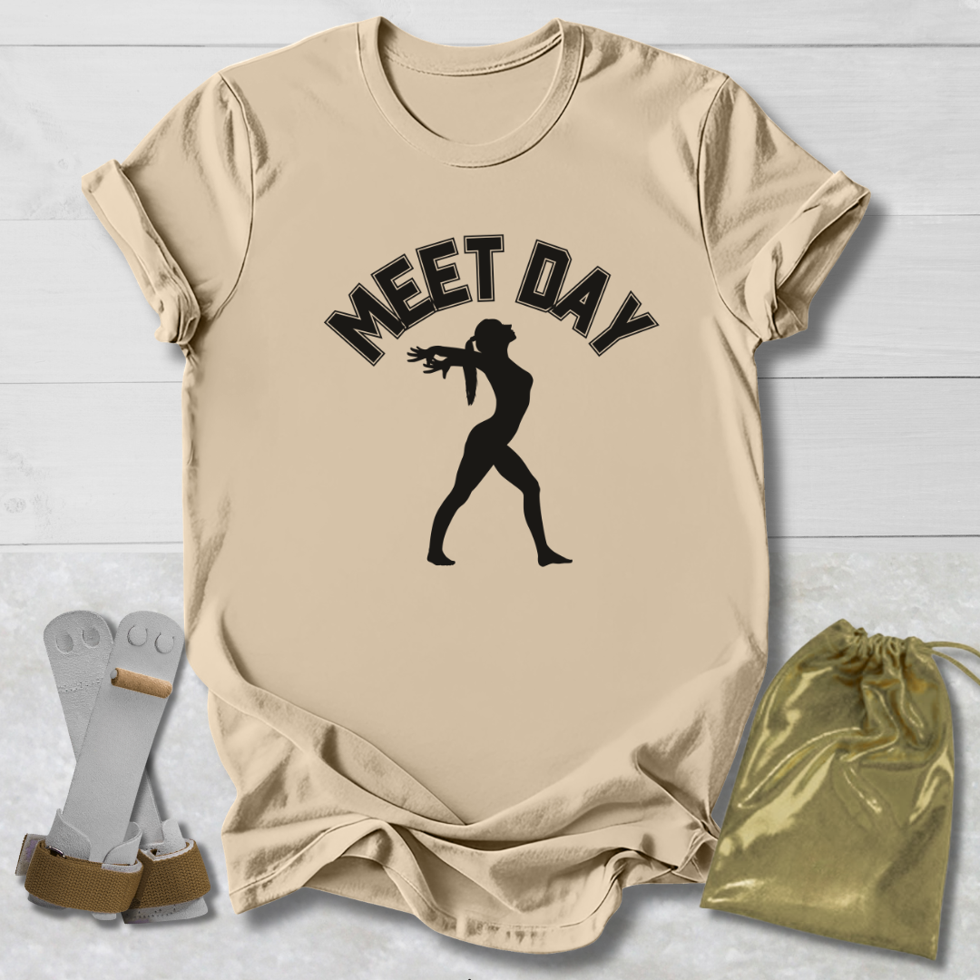 Beige t-shirt with black gymnast graphic and Meet Day text, socks, and drawstring bag on a light wooden surface.