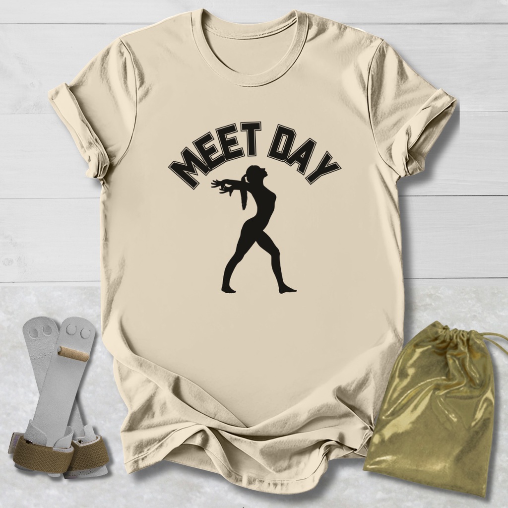 Beige t-shirt with black gymnast graphic and Meet Day text, socks, and drawstring bag on a light wooden surface