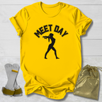 Yellow t-shirt with black gymnast graphic and Meet Day text, socks, and drawstring bag on a light wooden surface.