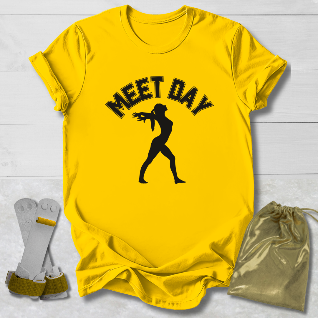 Yellow t-shirt with black gymnast graphic and Meet Day text, socks, and drawstring bag on a light wooden surface.