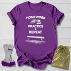 Purple t-shirt with 'Homework Practice Repeat' text and graphic, socks, and drawstring bag on a light wooden surface.