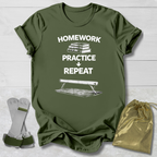 Green t-shirt with 'Homework Practice Repeat' text and graphic, socks, and drawstring bag on a light wooden surface.