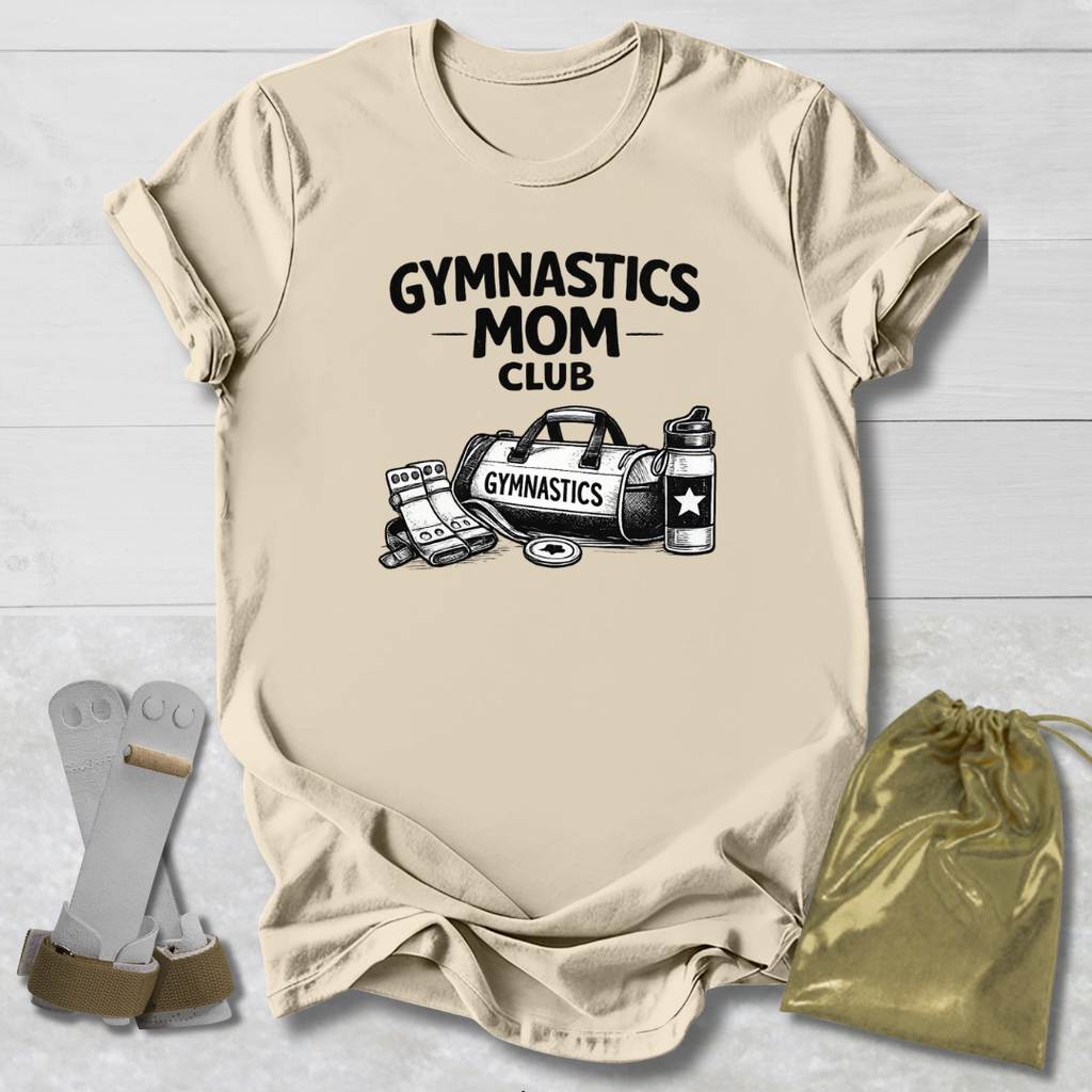 Beige t-shirt with 'Gymnastics Mom Club' text and graphics on a light wooden surface.