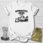 White t-shirt with 'Gymnastics Mom Club' text and graphics on a wooden surface with socks and a drawstring bag.
