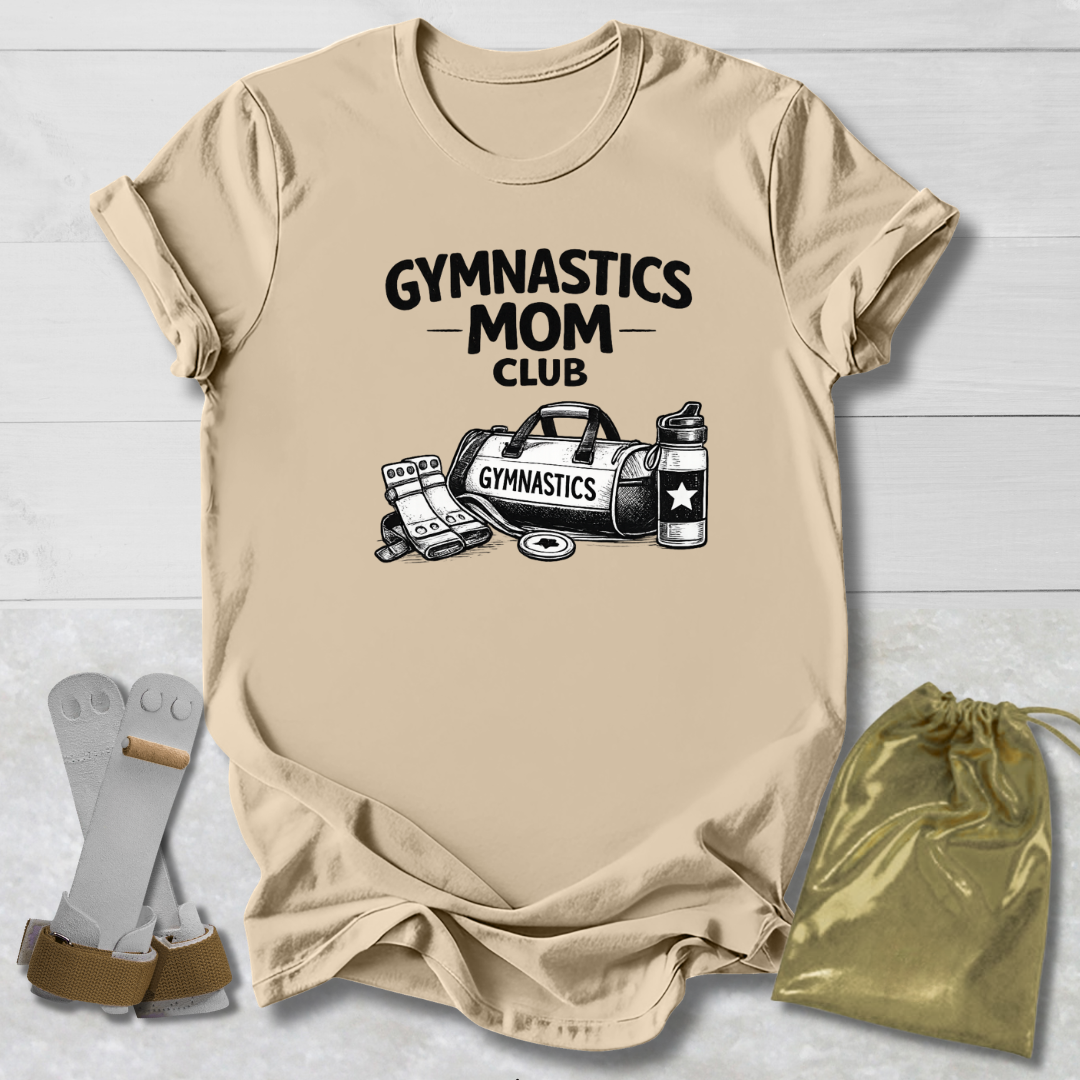 Beige t-shirt with 'Gymnastics Mom Club' text and graphics on a light wooden surface.
