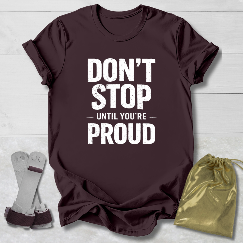 Maroon t-shirt with 'Don't Stop Until You're Proud' text, socks, and drawstring bag on a light wooden surface.