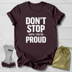Maroon t-shirt with 'Don't Stop Until You're Proud' text, socks, and drawstring bag on a light wooden surface.