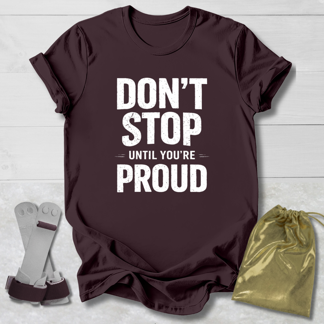 Maroon t-shirt with 'Don't Stop Until You're Proud' text, socks, and drawstring bag on a light wooden surface.