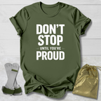 Green t-shirt with 'Don't Stop Until You're Proud' text, socks, and drawstring bag on a light wooden surface.