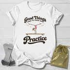 White t-shirt with 'Good Things Come to Those Who Practice' graphic on a wooden surface with socks and a drawstring bag.