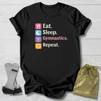 Black t-shirt with 'Eat. Sleep. Gymnastics. Repeat.' text and icons on a wooden surface with socks and a drawstring bag.