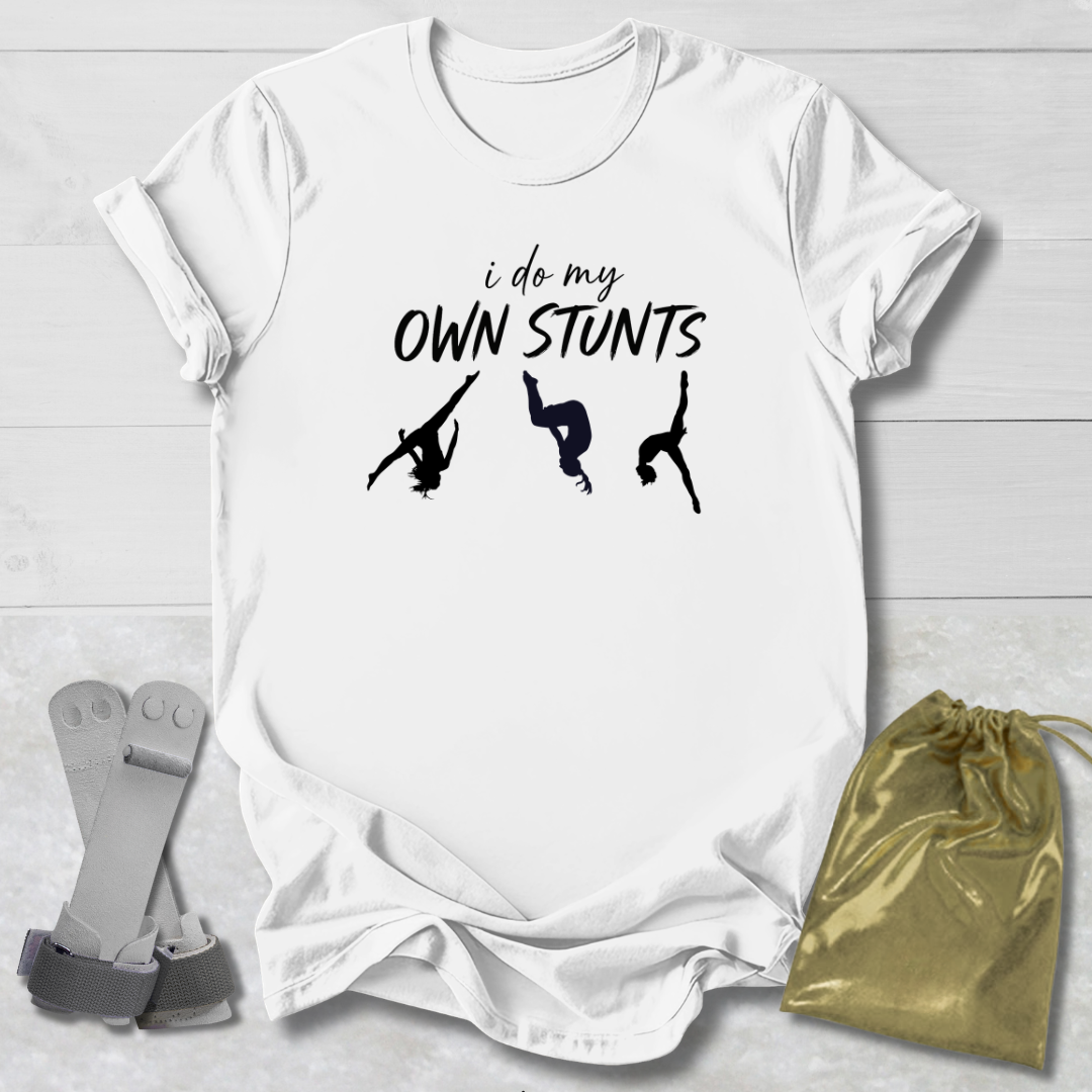 White t-shirt with 'I do my own stunts' text and silhouettes on a light wooden surface.