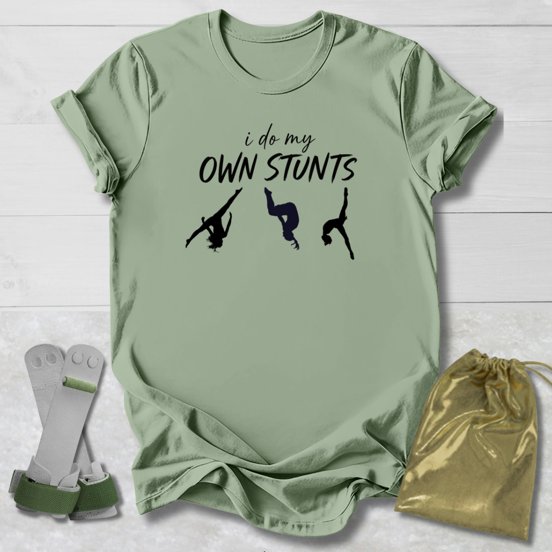 Green t-shirt with 'i do my own stunts' text and silhouettes, socks, and drawstring bag on a light wooden surface.