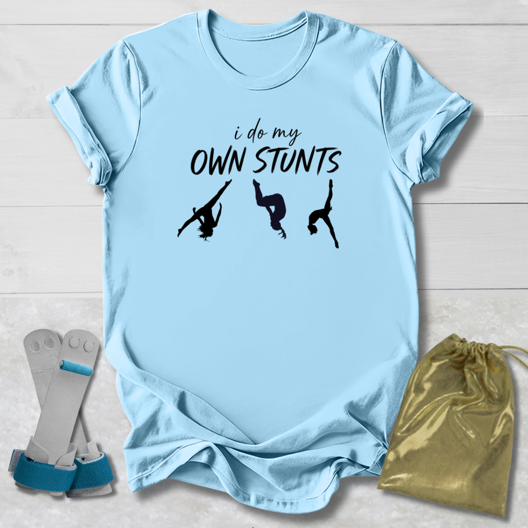 Light blue t-shirt with 'i do my own stunts' text and graphic, paired with socks and a drawstring bag on a light wooden surface.