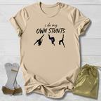 Beige t-shirt with 'i do my own stunts' text and graphic on a light wooden surface.