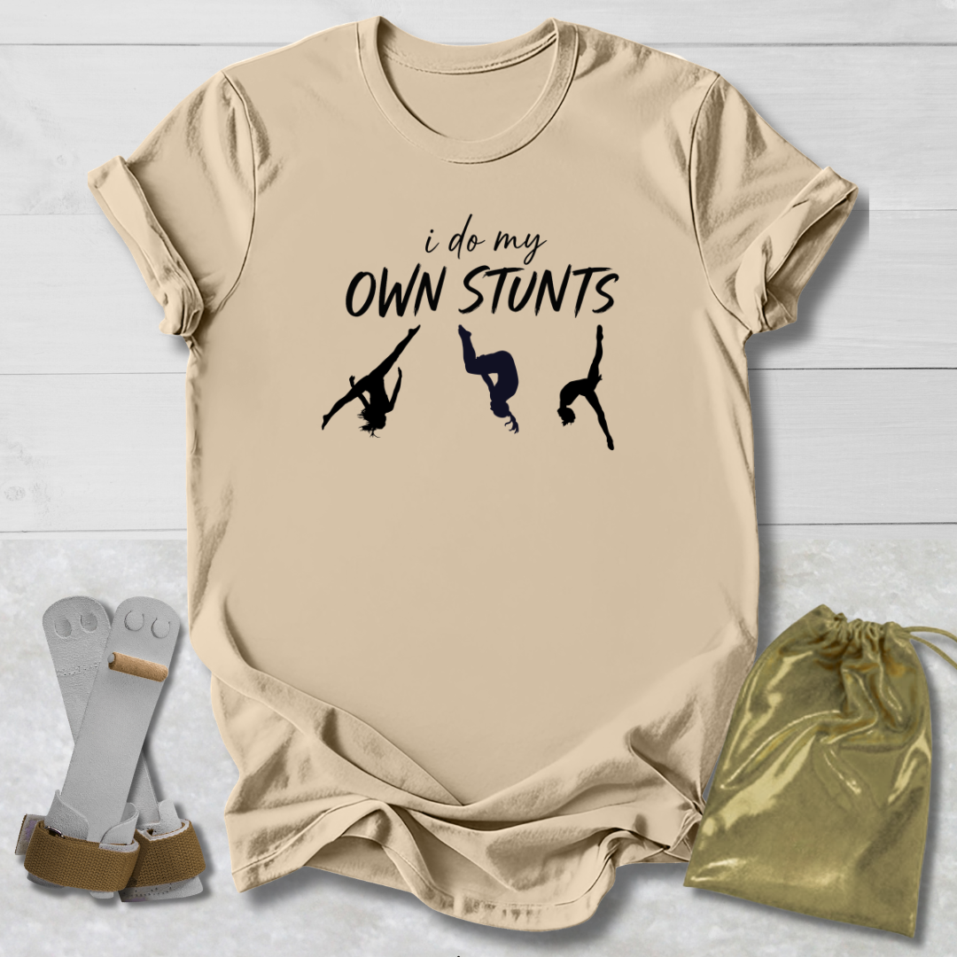 Beige t-shirt with 'i do my own stunts' text and graphic on a light wooden surface.