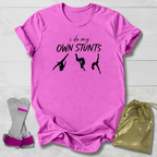 Pink t-shirt with 'i do my own stunts' text and silhouettes, socks, and drawstring bag on a light wooden surface.