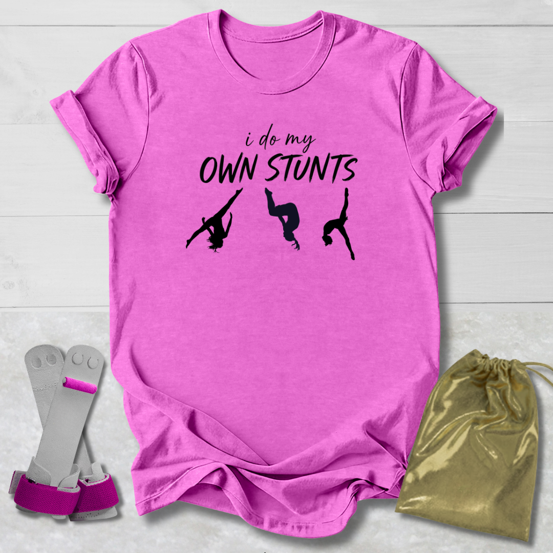 Pink t-shirt with 'i do my own stunts' text and silhouettes, socks, and drawstring bag on a light wooden surface.