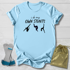Light blue t-shirt with 'i do my own stunts' text and graphic, paired with socks and a drawstring bag on a light wooden surface.