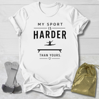 White t-shirt with 'My sport is harder than yours' text on a wooden surface with socks and a drawstring bag.