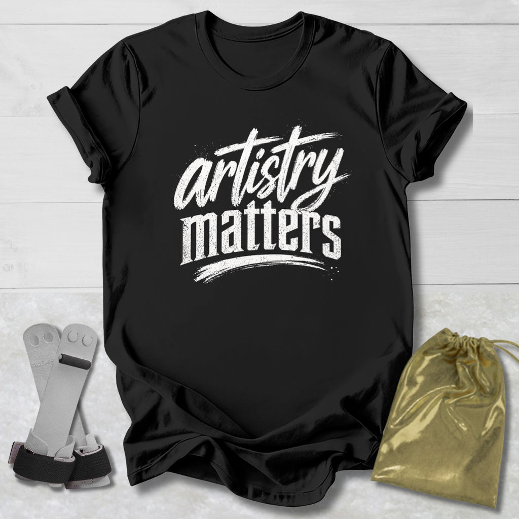 Black t-shirt with 'artistry matters' text on a light wooden surface with socks and a drawstring bag.