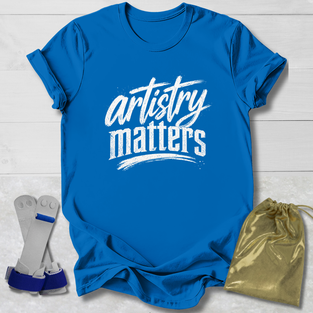 Blue t-shirt with 'artistry matters' text, socks, and a drawstring bag on a light wooden surface.