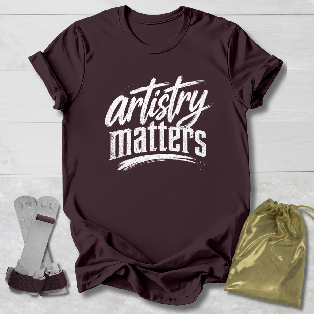 Maroon t-shirt with 'artistry matters' text, socks, and a drawstring bag on a light wooden surface.