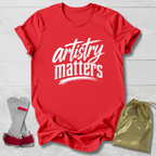 Red t-shirt with 'artistry matters' text, socks, and drawstring bag on a light wooden surface