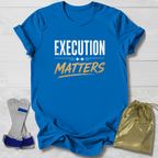 Blue t-shirt with 'Execution Matters' text on a wooden surface with socks and a drawstring bag.