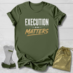 Green t-shirt with 'Execution Matters' text, socks, and drawstring bag on a light wooden surface