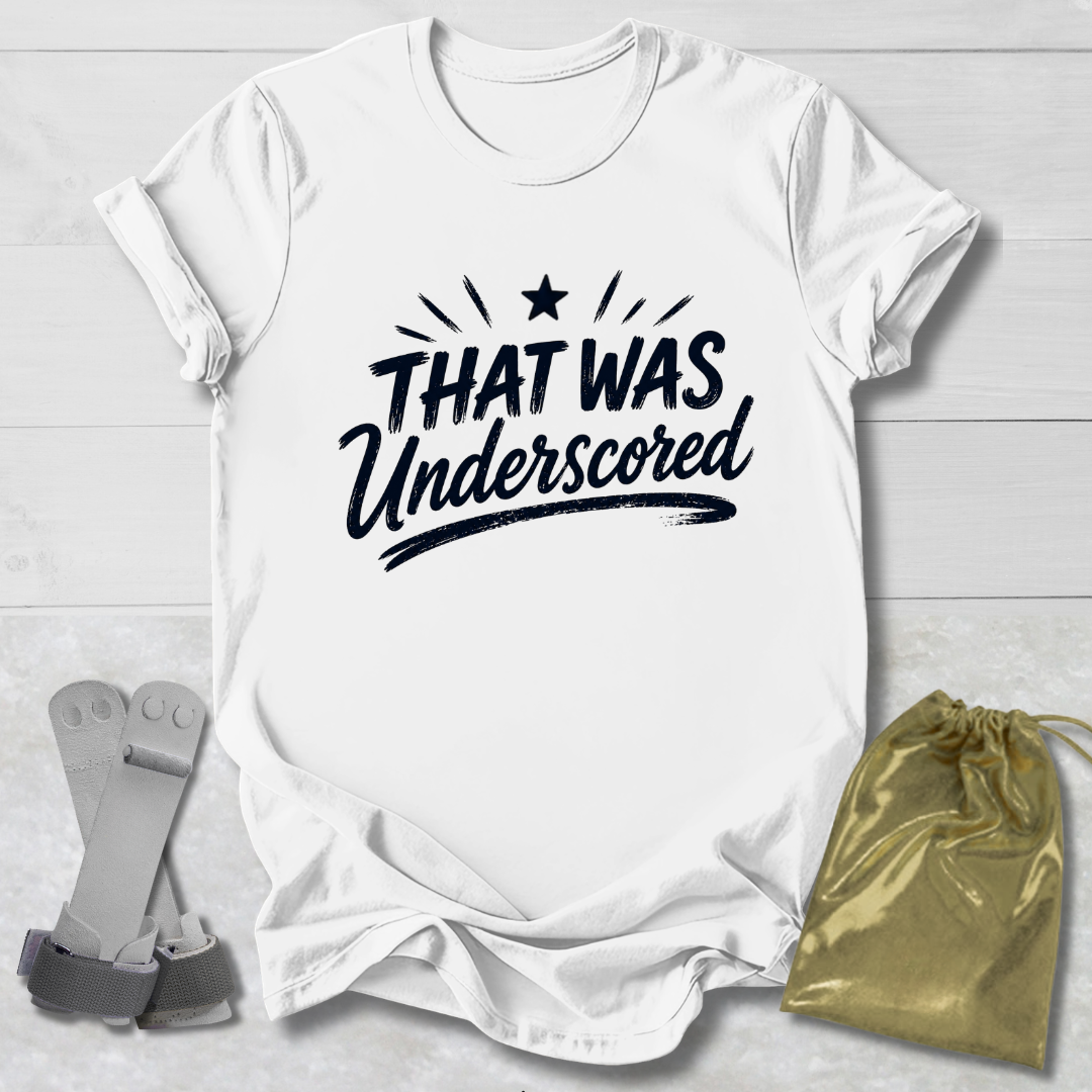White t-shirt with 'THAT WAS Underscored' text on a light wooden surface with socks and a drawstring bag.