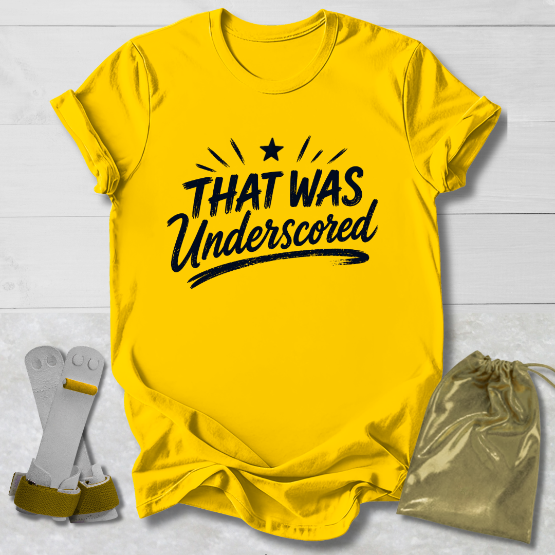 Yellow t-shirt with 'THAT WAS Underscored' text, socks, and drawstring bag on a light wooden surface.