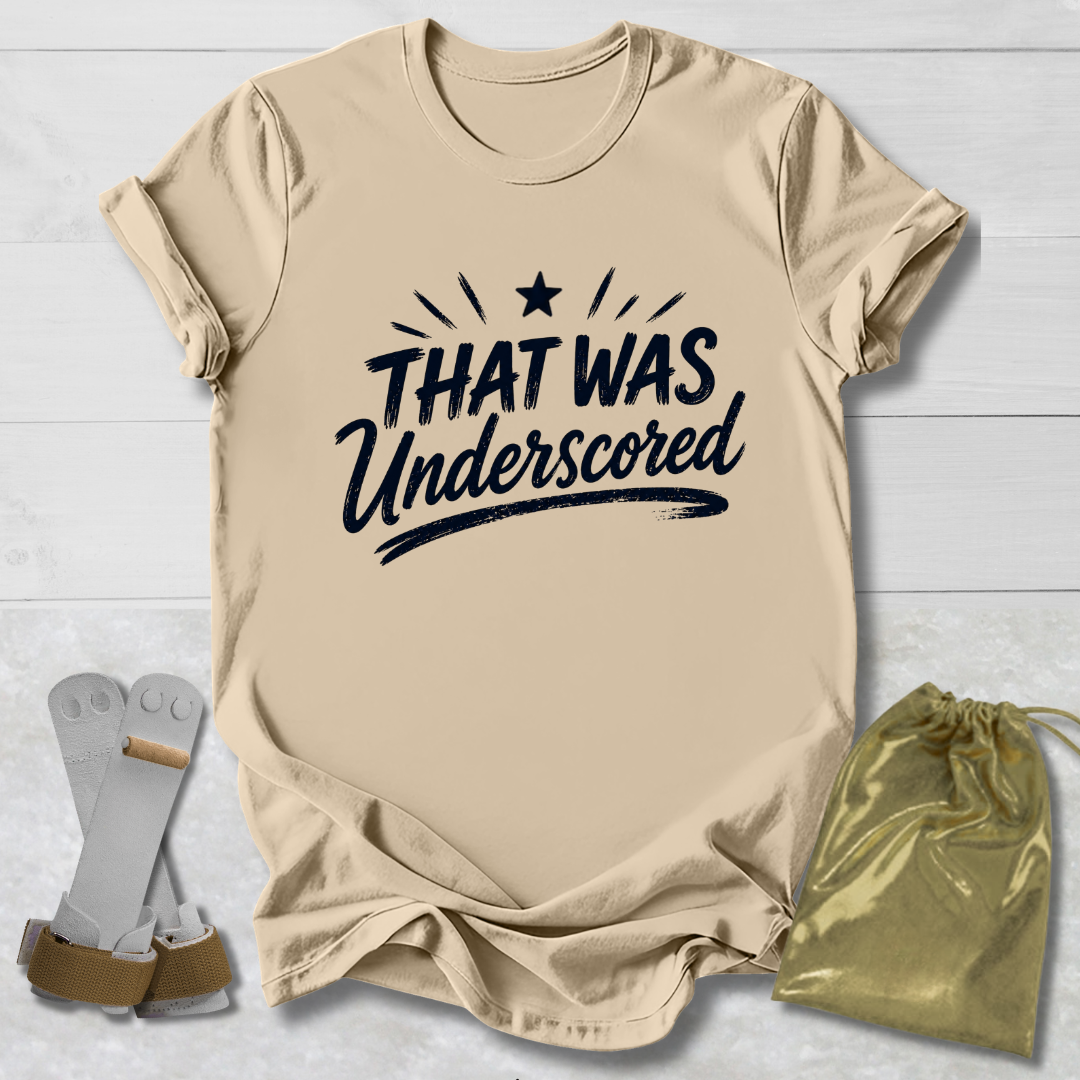 Beige t-shirt with 'THAT WAS Underscored' text, socks, and drawstring bag on a light wooden surface