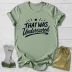 Gray t-shirt with 'THAT WAS Underscored' text, socks, and drawstring bag on a light wooden surface