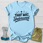 Light blue t-shirt with 'THAT WAS Underscored' text, socks, and drawstring bag on a light wooden surface.