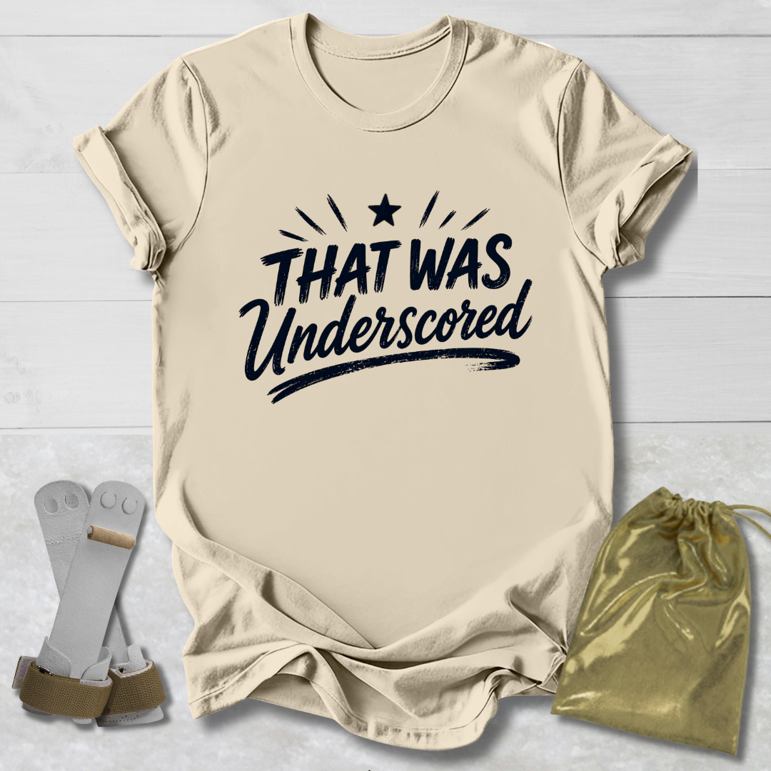 Beige t-shirt with 'THAT WAS Underscored' text, socks, and drawstring bag on a light wooden surface.