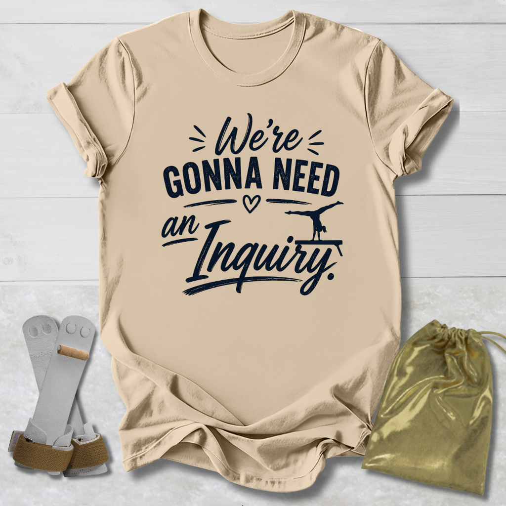 Beige t-shirt with text 'We're Gonna Need an Inquiry' on a light wooden surface with socks and a drawstring bag.